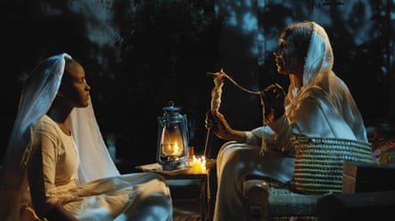 A still from a film, with a young girl talking to her grandmother as they sit next to a lamp at night