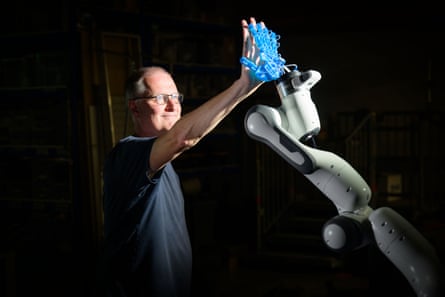 A man in glasses and a dark shirt high-fives a robotic hand.
