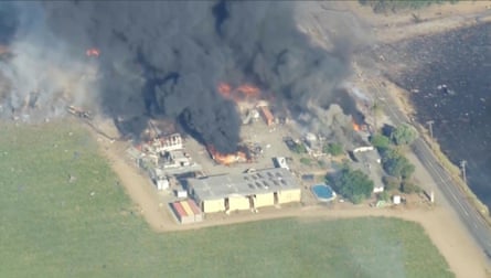 Aerial view of smoke and flames rising from a bunch of buildings alongside a field