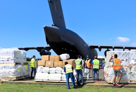 Pallets loaded with boxes behind a C-17 aircraft with men in high-vis vests