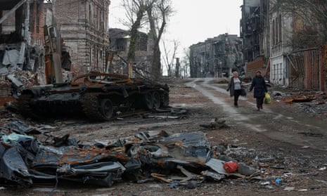 People walk near a destroyed tank and damaged buildings in Mariupol.