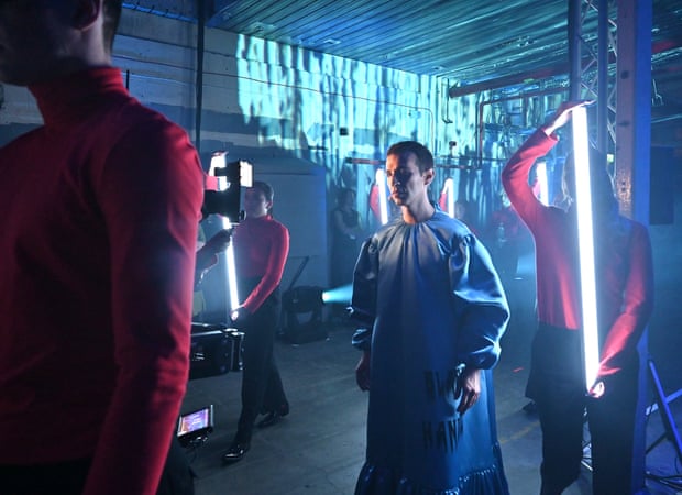 People hold strip-lights while a person in a puff-sleeve dress walks between them
