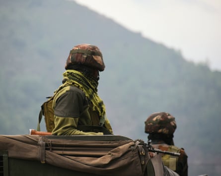 Two people in military uniform are seen from behind riding in an Indian army vehicle
