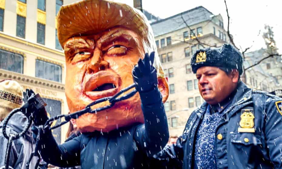 Figure wearing a huge Donald Trump head in a mock arrest in New York