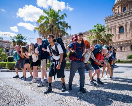 Ten people with backpacks prepare to race in a sunny square in Italy