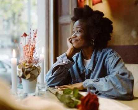 A woman on a date sat at a table near a window, smiling towards someone off camera