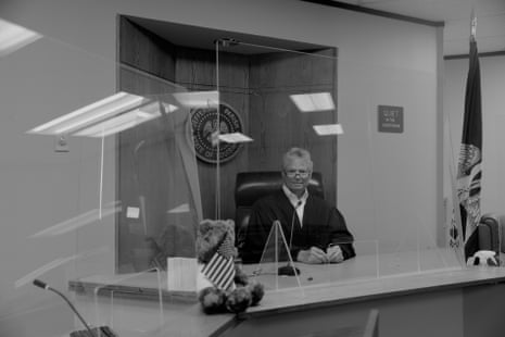 A judge sits in a courtroom with a US flag at the side