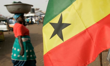 A woman food seller walks past a Ghanaian flag flying in the wind in Tamale, Ghana