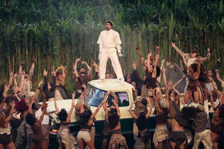 Bad Bunny performing in white suit atop white pick-up surrounded by people