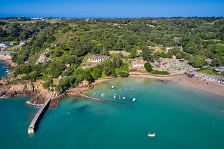 An aerial shot of blue waters in a picturesque bay, with forests in the background