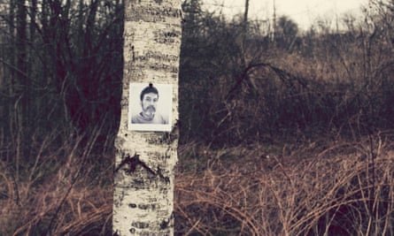 A tree trunk in a wood with a  black and white photo of a missing man on it
