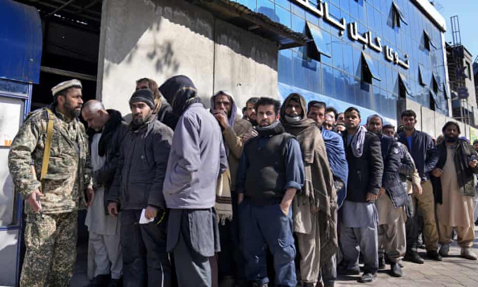 A Taliban fighter stands guard in front of people waiting to enter a bank in Kabul, Afghanistan