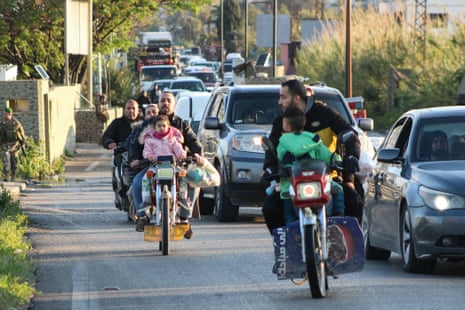 पुरुषों, महिलाओं और बच्चों के साथ तीन मोटरबाइकें कारों की कतार से गुजर रही हैं।