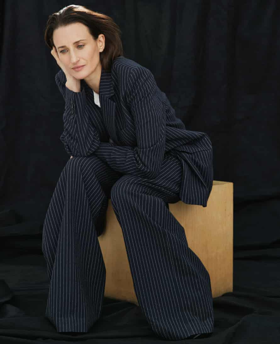 Actor Camille Cottin in prinstripe suit, sitting on wooden cube