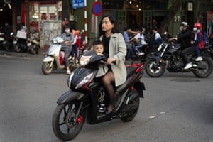 A woman in a jacket drives a motorbike while a young boy sits in front.