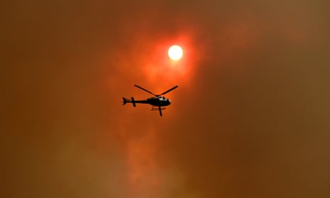 A spotter helicopter flies through thick bushfire