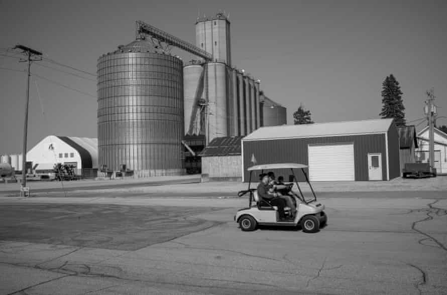 A family drives a golf cart past a silo and other farm buildings in downtown Williams.