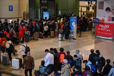 Mask-clad passengers wait in a line after arriving at the railway station in Wuhan