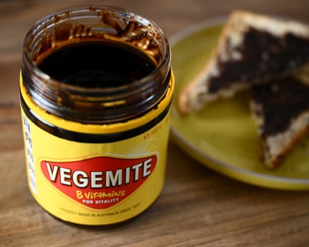 An open jar of Vegemite, with a piece of toast covered in the stuff on a green plate.