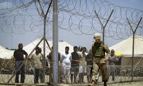 A US soldier walks past Iraqi detainees standing behind a wired fence, at Abu Ghraib prison outside Baghdad in 2004. 