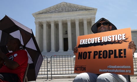 A man sits in a chair in front of the supreme court in Washington DC holding an orange sign that reads "Execute justice, not people!"