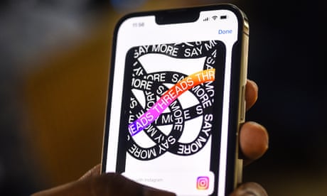 Hand holds a mobile phone displaying the Threads app logo.