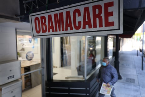 A masked man walks past a Miami insurance agency beneath a large 'Obamacare' sign