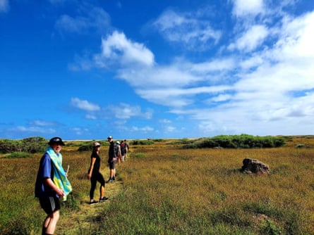 Three adults posing on a grassy hiking trail in Western Australia against a blue sky.