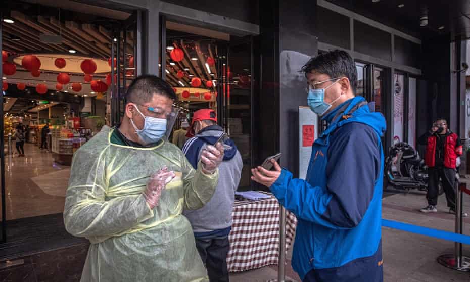 A worker in a protective outfit checks health QR codes of a man at the entrance of a shopping mall in Wuhan