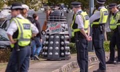 Police at a protest against the DSEI arms fair, looking at protester in dalek costume with sign reading: 'Stop killing people!'