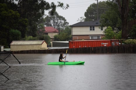 A child paddles a canoe by Church Street, Windsor, NSW.