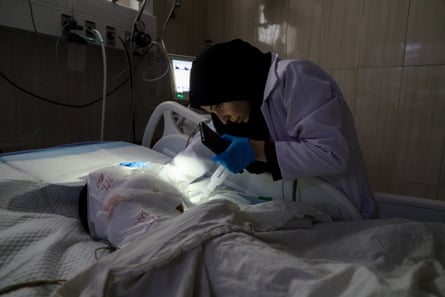 A health worker uses the light from her phone in Gaza’s al-Aqsa Martyrs hospital to check on a patient