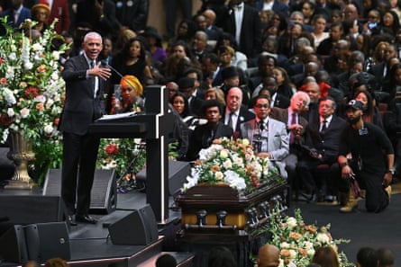 a man in suit speaking at lectern as people seated in crowd look on
