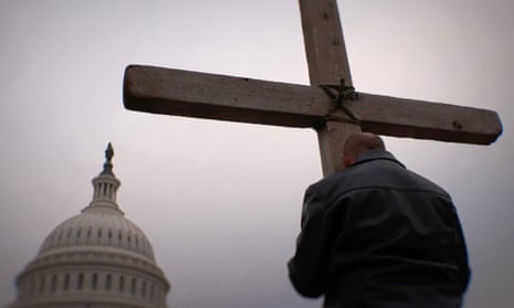 a man holds a cross in front of a cloudy sky and the domed Capitol building in Washington