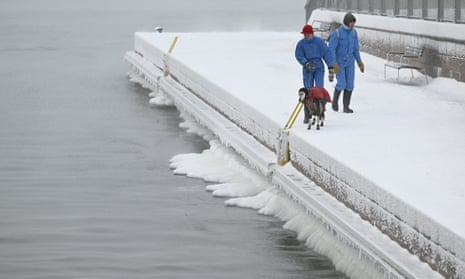 A warmly-dressed couple walk with their warmly-dressed pet dog on a pier by the sea in southern Helsinki.