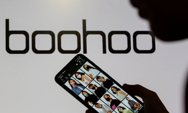 Someone poses with a smartphone showing the Boohoo app in front of the Boohoo logo on display
