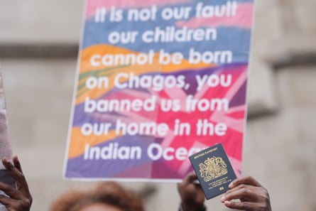 Someone holds up a British passport next to a sign that says: it is not our fault our children cannot be born on Chagos, you banned us from our home in the Indian Ocean