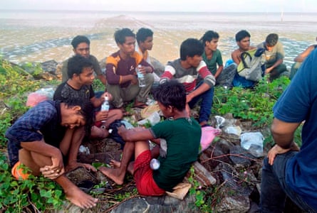 Eleven young south Asian men sitting on the ground beside a large beach