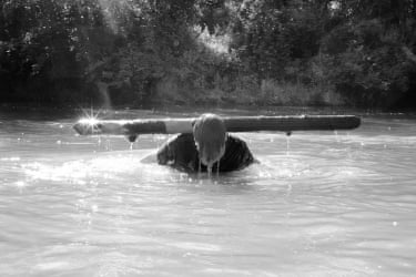 A young man stands up in the river with a log on his shoulders
