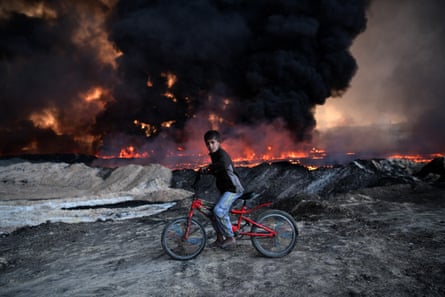 A boy pauses as he cycles past an oilfield set on fire by retreating Isis fighters in Qayyarah, Iraq