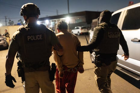 Homeland Security taskforce officers escort a handcuffed suspect along a street at night.