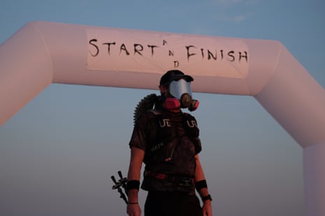 man in gas mask stands in front of sign saying 'start and finish'