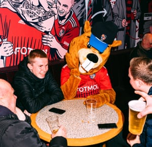 Joel Golby as Bertie the Beaver sitting at a table with fans drinking beer