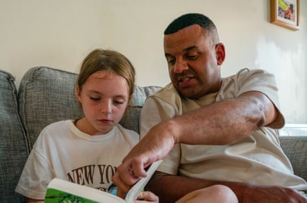 A man and a nine-year-old girl read a book together on a sofa