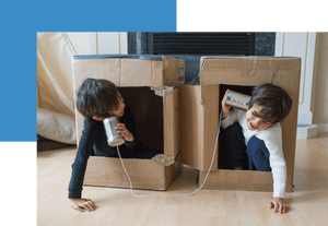 Two boys in cardboard boxes playing with can and string phones