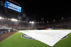 A tarp covers the field, a sign announces the postponement of the game and fireworks explode at the MLB Speedway Classic.
