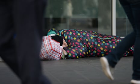 People walking past a homeless person in a sleeping bag on the floor