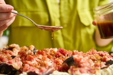 A spoon drizzling a pomegranate dressing over a platter of figs.