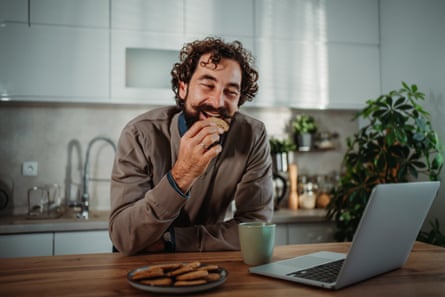 Man laughing and eating cookie while working from home on his laptop