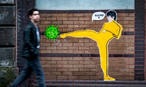 A member of the public walks past a piece of street art by ‘Palley’ that features Bruce Lee kicking a coronavirus molecule in Glasgow’s East End